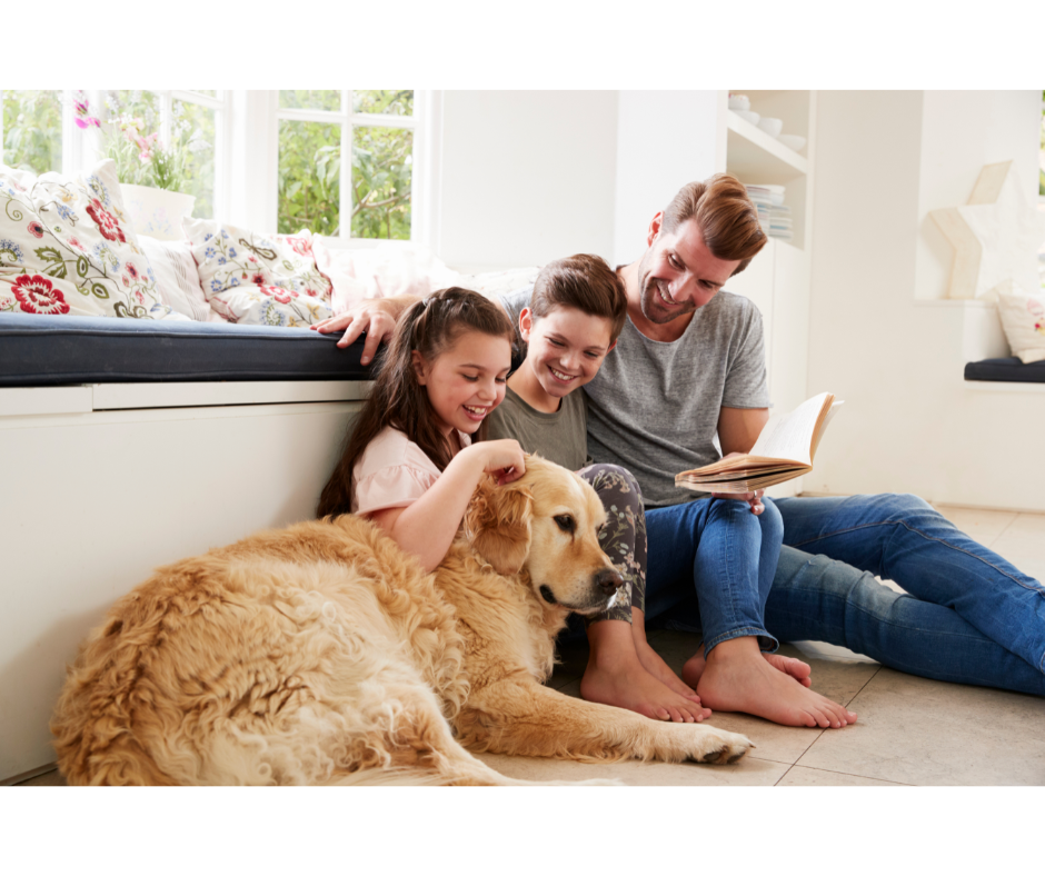 man reading book with his kids and dog sitting on floor