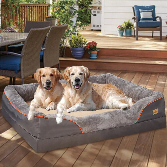 Two large dogs lying on a jumbo orthopedic dog bed with a gray cover and orange detailing, placed on a wooden deck.